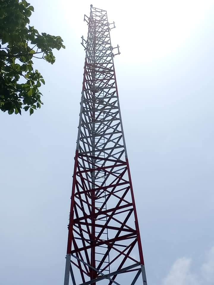 Red-and-white lattice tower with mounted antennas photographed against a bright sky