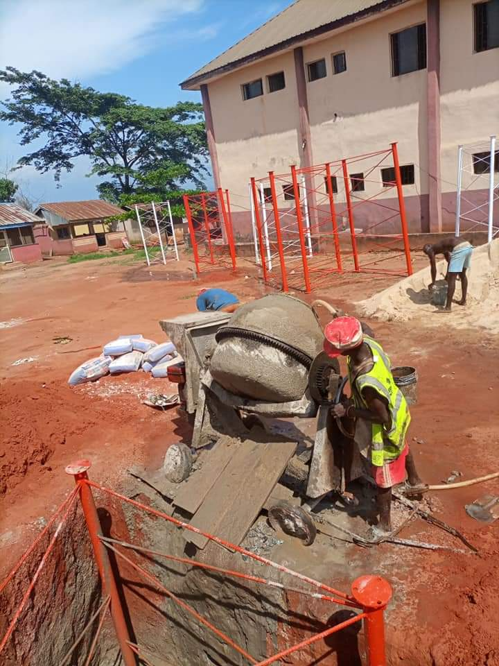 Workers operating a cement mixer beside red-and-white tower steel sections at a site yard